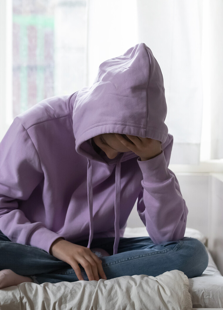 Junge Frau sitzt nachdenklich auf dem Bett