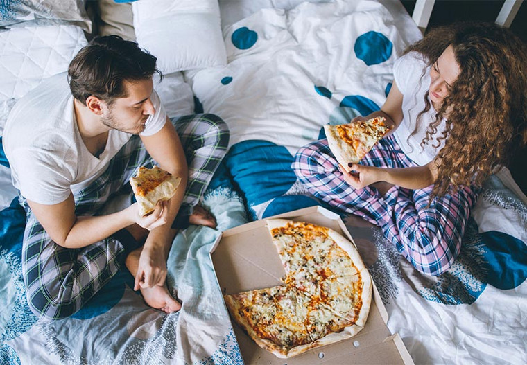 Paar isst Pizza im Bett