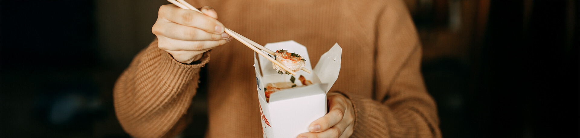 Mensch isst mit Stäbchen aus Papierbox