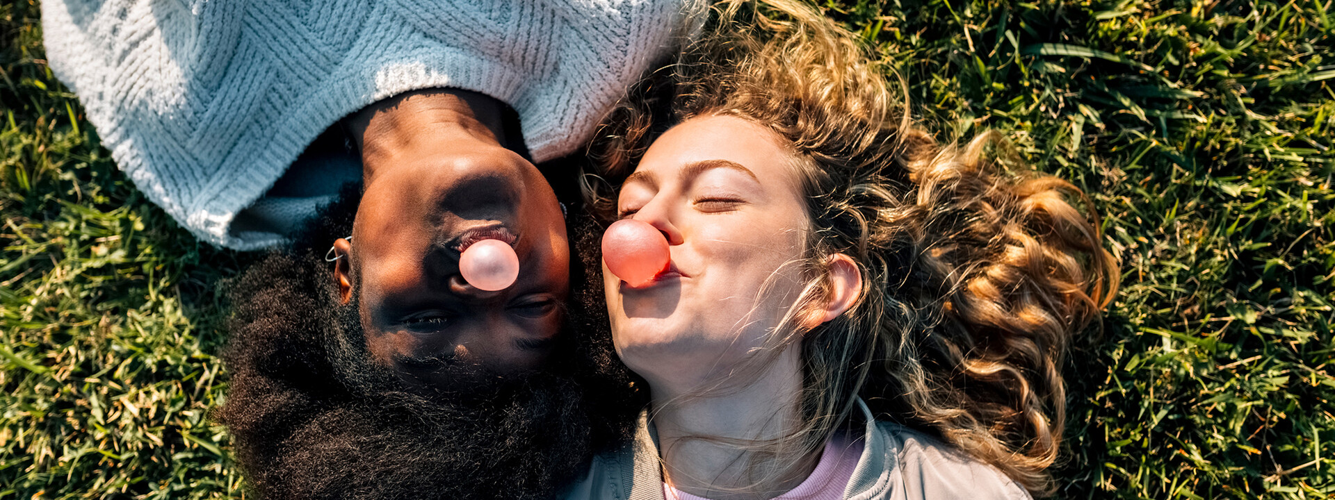 Zwei junge Frauen liegen im Gras und machen Kaugummiblasen