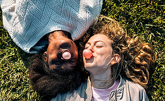 Zwei junge Frauen liegen im Gras und machen Kaugummiblasen