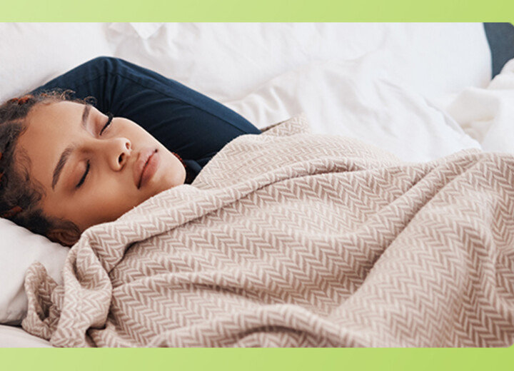 Studentin schläft im Bett. Neben ihr liegen Lernmaterialien und ihr Handy
