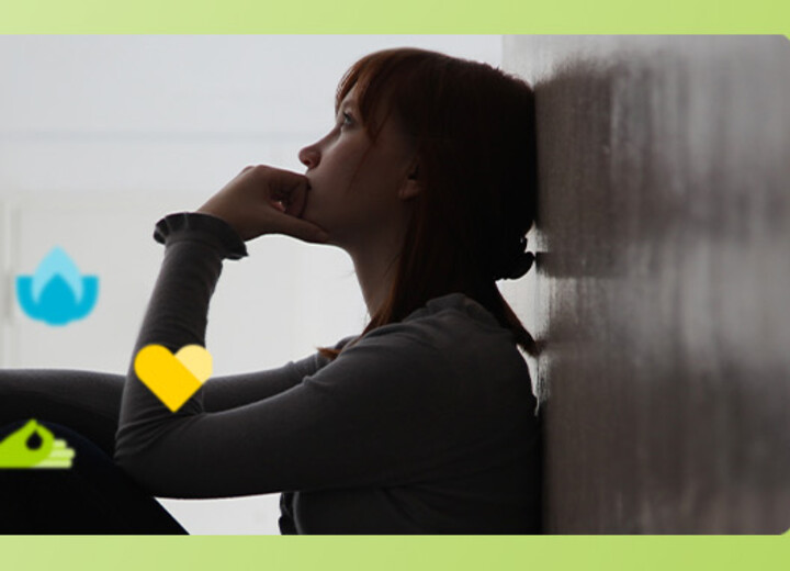 Junge Frau sitzt nachdenklich auf dem Boden gegen eine Wand gelehnt.