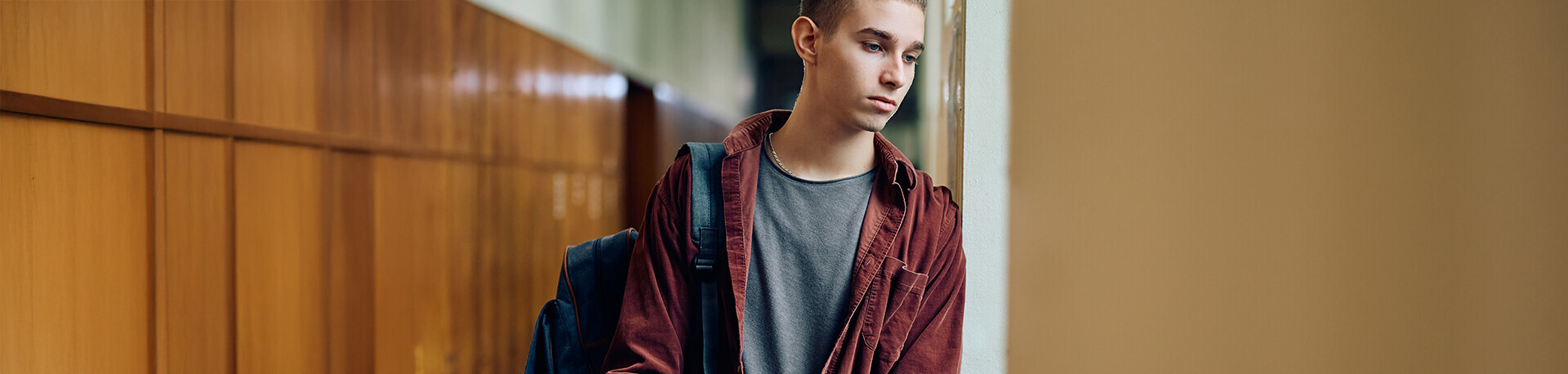 Junger Mann mit Karohemd und Büchern in der Hand lehnt gedankenverloren an einer Glasscheibe