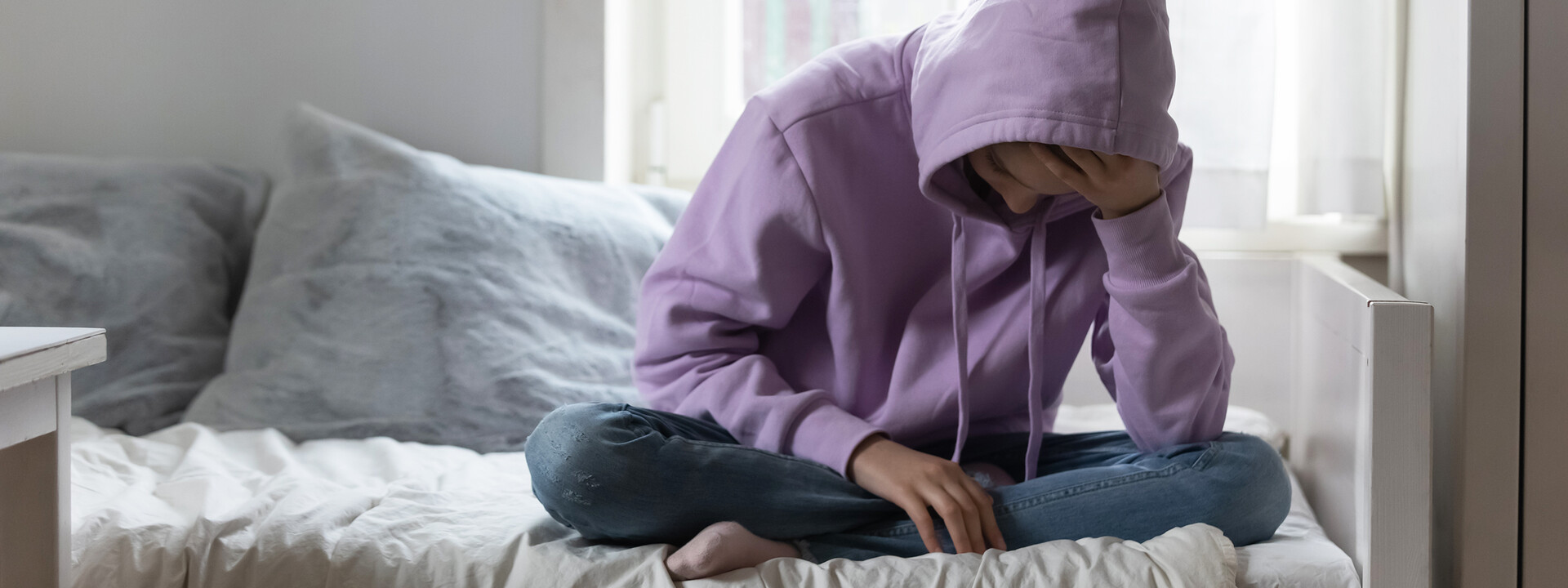 Junge Frau sitzt nachdenklich auf dem Bett