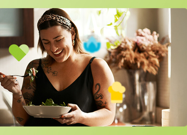 Junge Frau steht in der Küche und sieht zufrieden aus, während sie einen Salat isst