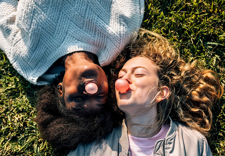 Zwei junge Frauen liegen im Gras und machen Kaugummiblasen