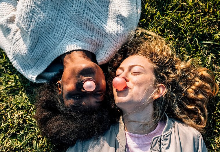 Zwei junge Frauen liegen im Gras und machen Kaugummiblasen