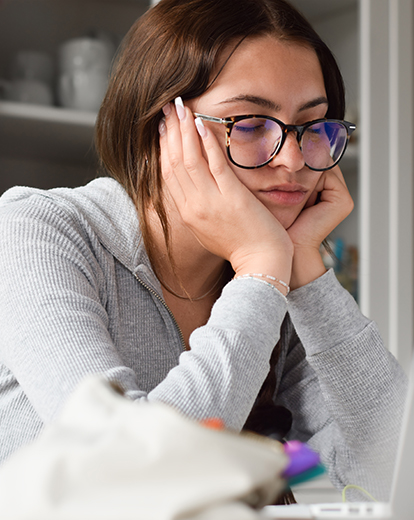 Eine Studentin schaut unkonzentriert und müde auf ihren Laptop.