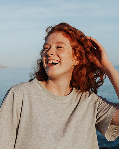 Junge Frau mit roten Haaren am Meer lacht