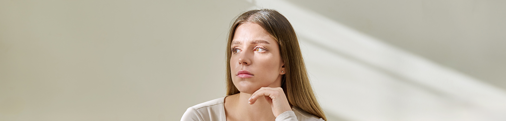 Junge Frau sitzt mit nachdenklichem Blick auf dem Bett