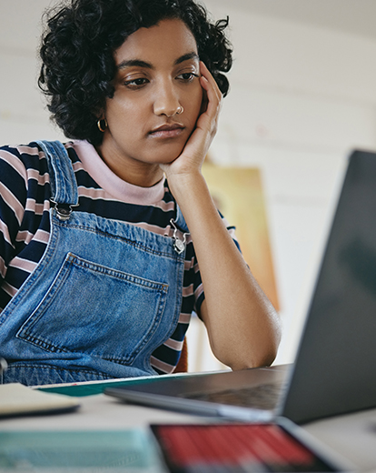 Frau hat Gesicht in eine Handfläche gestützt und schaut in ihren Laptop