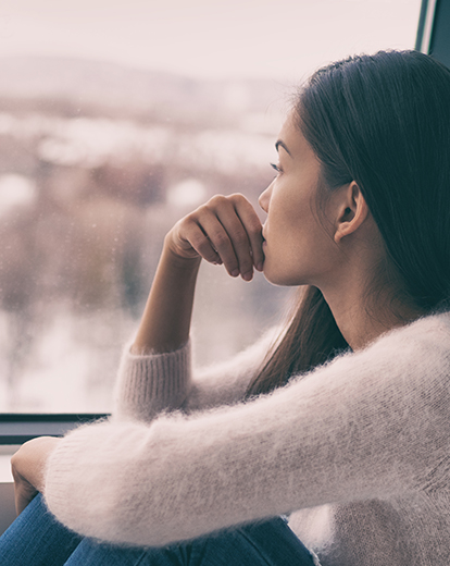 Frau schaut betrübt aus dem Fenster