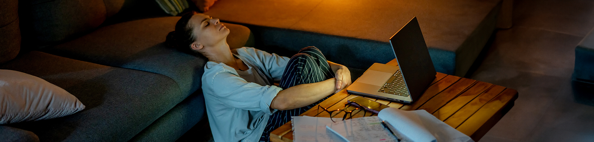 Frau sitzt zusammengekauert auf dem Boden vor ihrem Laptop 