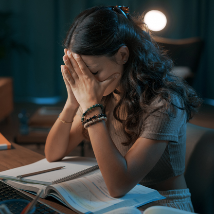 Frau hat das Gesicht in ihre Hände gestützt und sitzt vor ihren Unterlagen
