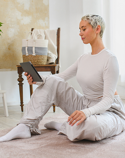 Frau sitzt in Jogginghose auf dem Boden und schaut in ihr IPad