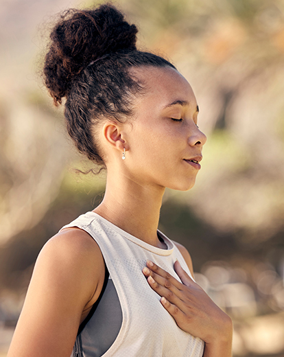Junge Frau steht mit geschlossenen Augen in der Natur