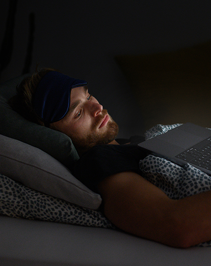 Junger Mann liegt im Bett und schaut auf seinen Laptop