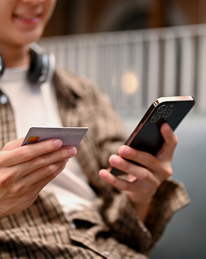 Person hält Kreditkarte in der einen und Handy in der anderen Hand