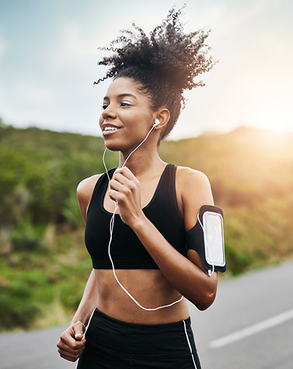 Frau mit Kopfhörern und Sportklamotten rennt auf einer Straße