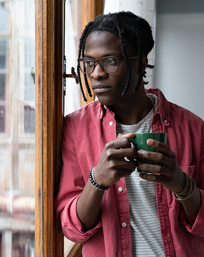 Mann mit Tasse in der Hand schaut nachdenklich aus dem Fenster