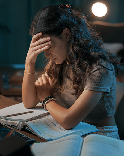 Eine Studentin sitzt am Schreibtisch. Sie wirkt erschöpft und verzweifelt. 