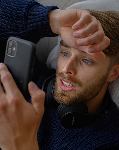 Mann mit verzweifeltem Gesichtsausdruck liegt im Bett und schaut auf sein Handy
