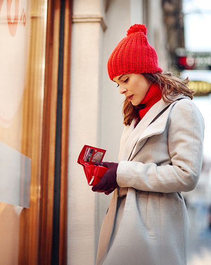 Frau im Winter schaut in ihr Portmonee vor einem Geschäft