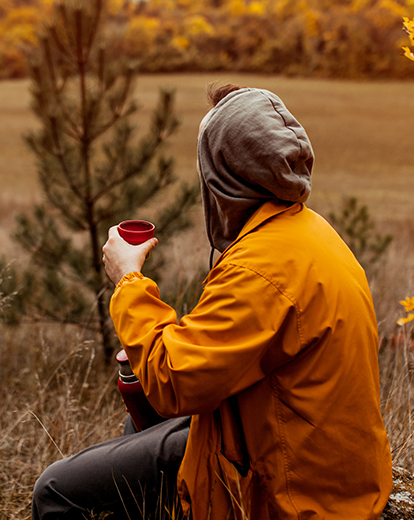 Mann sitzt mit Regenjacke und Tasse in der Natur