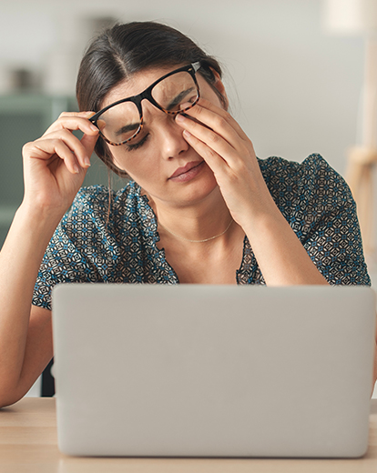 Eine junge Frau sitzt vor ihrem Laptop und reibt sich müde die Augen.