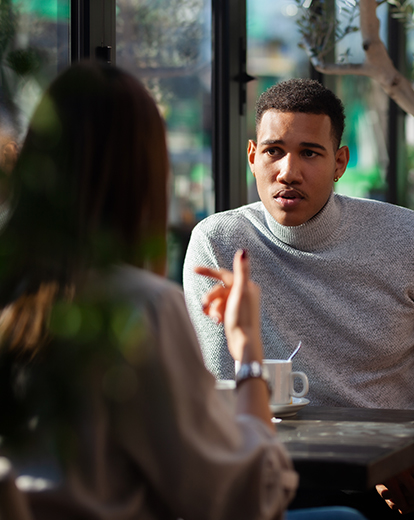 Junger Mann sitzt nachdenklich draußen zusammen mit einer Frau in einem Café