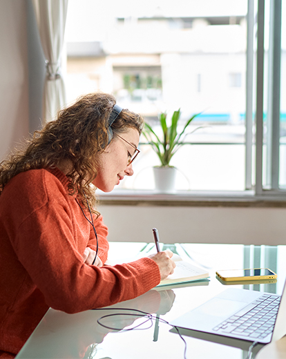 Studentin sitzt am Schreibtisch und schreibt auf ein Papier