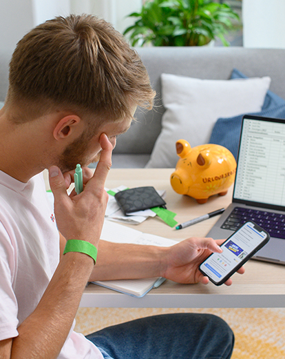 Mann sitzt vor seinem Laptop und seinem Handy und grübelt über Tabellen