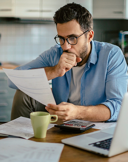 Mann sitzt in der Küche an einem Tisch vor Papieren