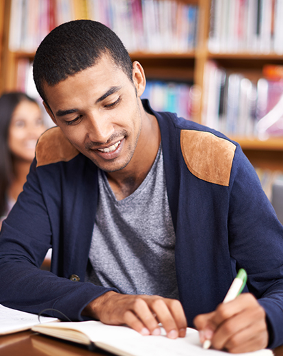 Junger Mann sitzt lachend im Unterricht und schreibt etwas auf Papier