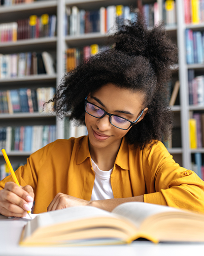 Frau sitzt in der Bibliothek vor einem Buch mit einem Stift in der Hand