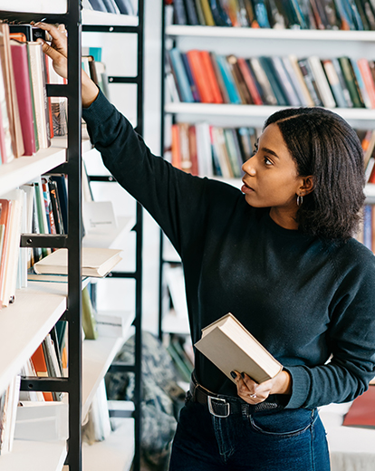 Studentin in einer Bibliothek vor einem Bücherregal