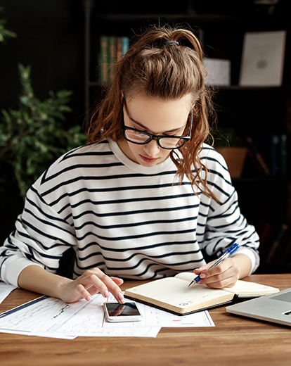 Junge Frau sitzt vor einem Buch und tippt in einen Taschenrechner