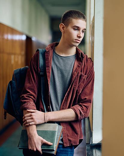 Junger Mann mit Karohemd und Büchern in der Hand lehnt gedankenverloren an einer Glasscheibe