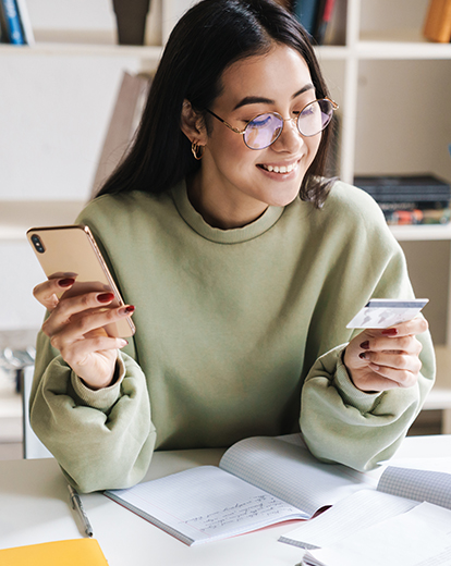 Lächelnde junge Frau mit Handy und Kreditkarte in der Hand