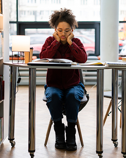 Studentin sitzt in Bibliothek und hat den Kopf in beide Hände gestützt