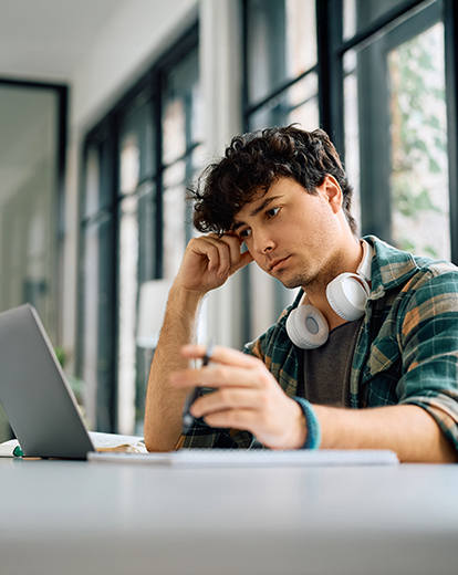 Junger Mann schaut nachdenklich in einen Laptop, den Kopf auf eine Hand gestützt