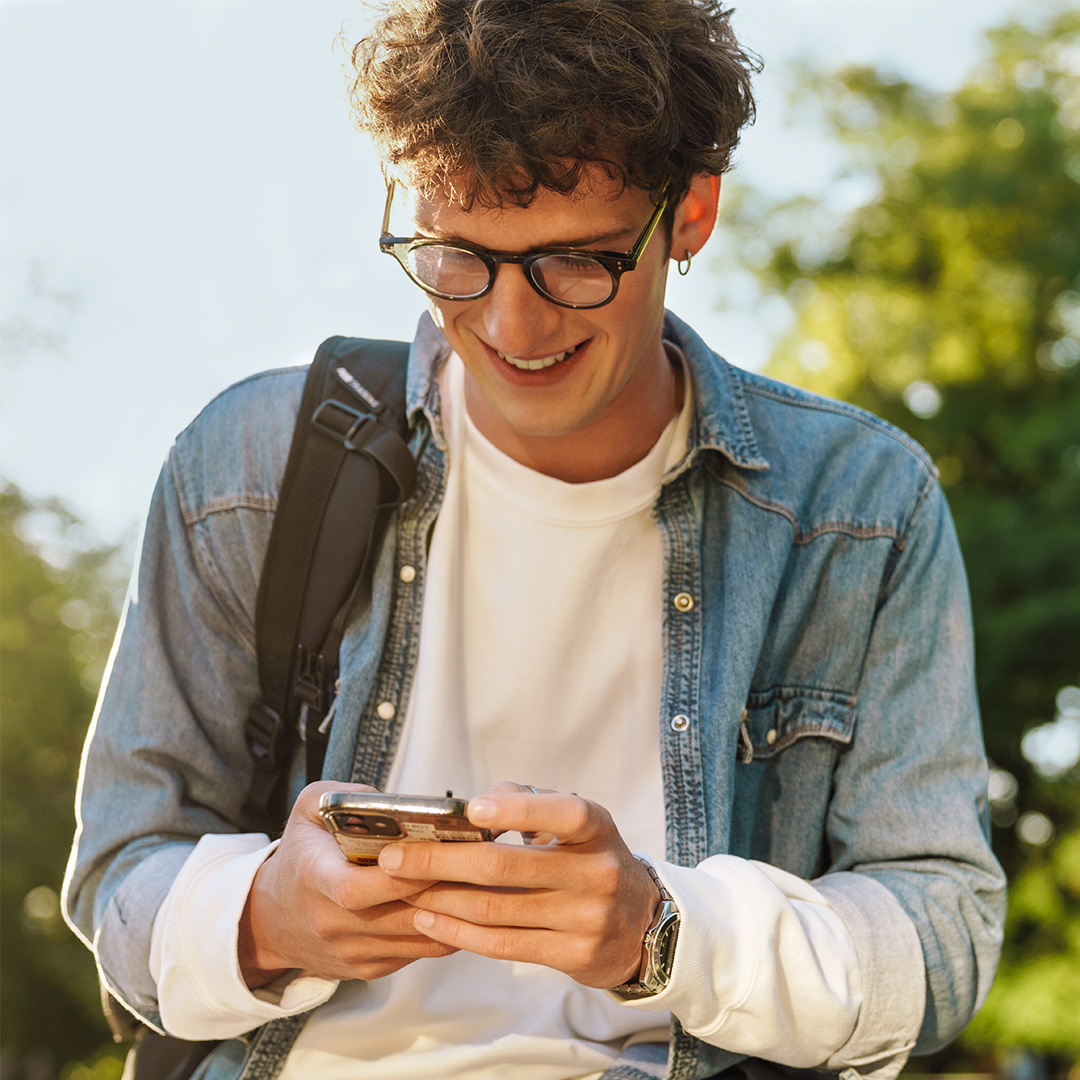 Ein Student lacht und tippt auf seinem Handy.